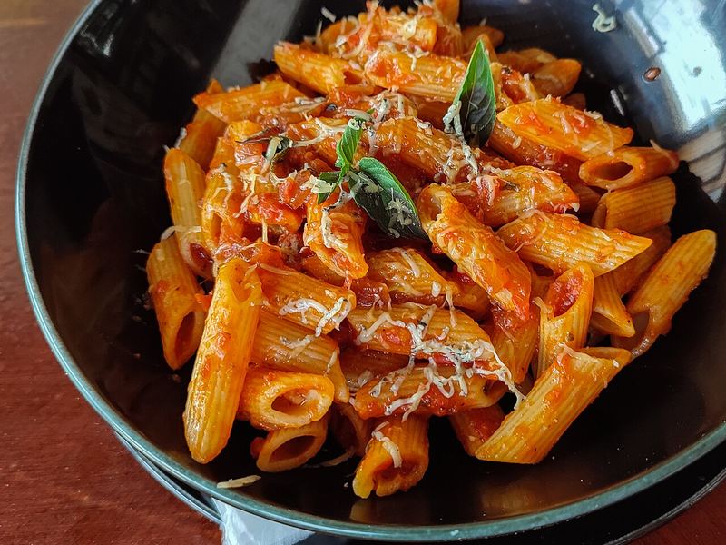 Penne em molho de tomate vermelho-vivo numa panela, com folhas de manjericão.