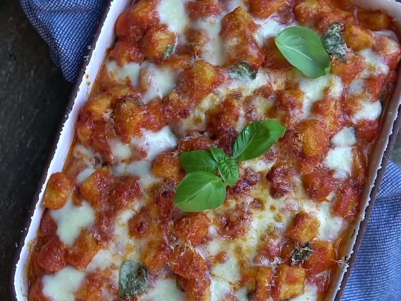 Travessa de nhoque gratinado com molho de tomate, mussarela derretida e folhas de manjericão.