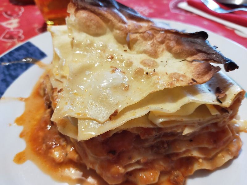 Fatia de lasanha à bolonhesa em pé no prato, com as camadas de massa e ragù à mostra.