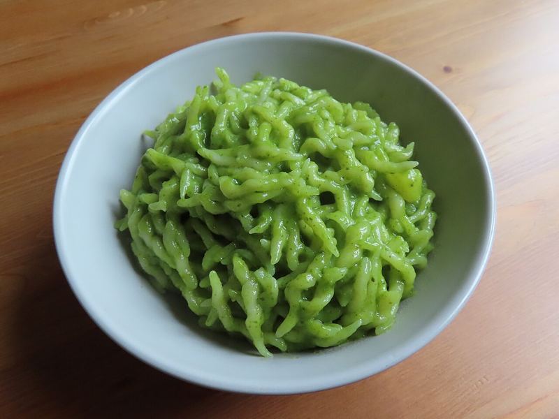 Trofie curtas cobertas de pesto verde-vivo numa tigela clara.