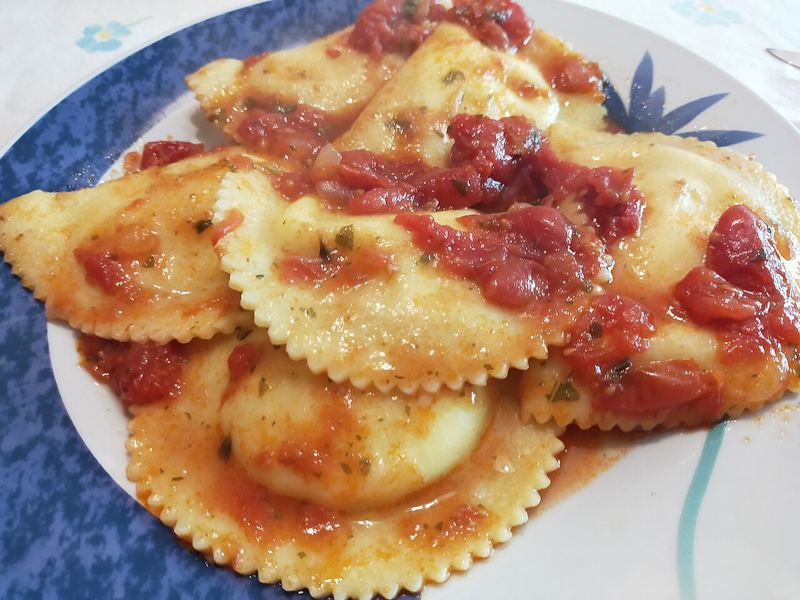 Ravioli quadrados de borda ondulada cobertos por molho de tomate e manjericão.
