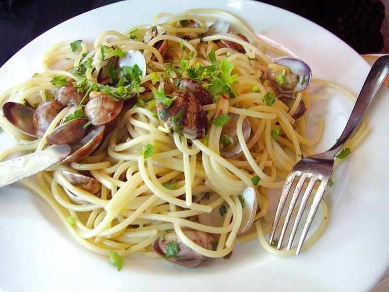 Spaghetti alle vongole com conchas abertas e salsinha picada, num prato branco.