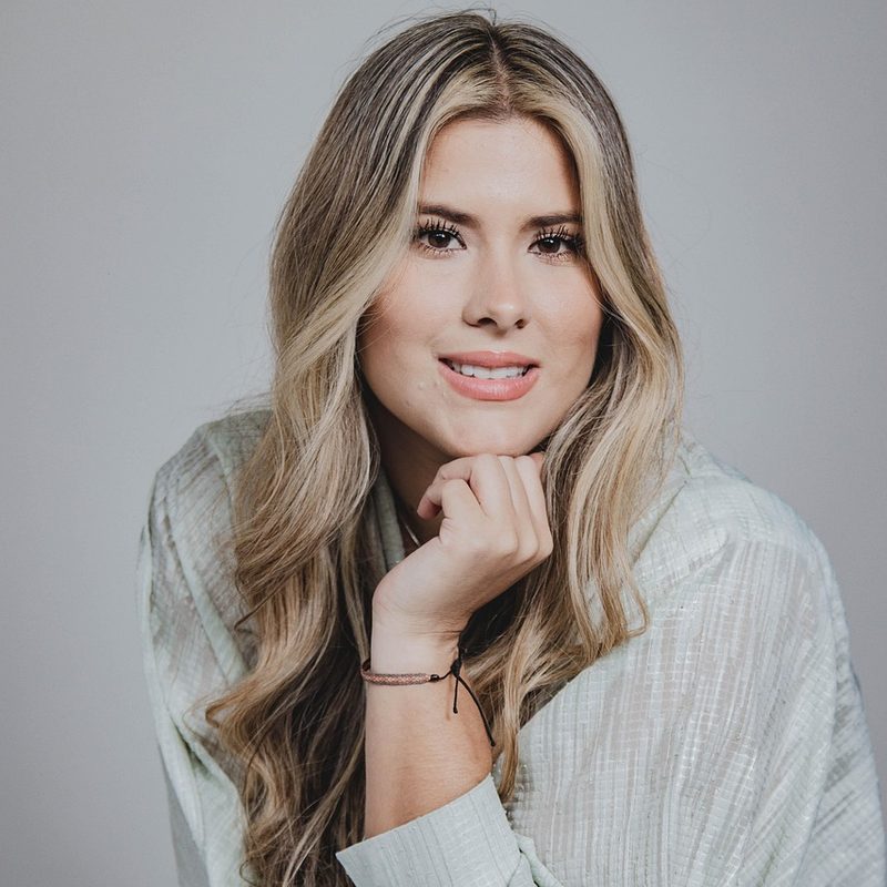Retrato de Helena Sartori, psicóloga, com blusa verde-sálvia sobre fundo neutro.